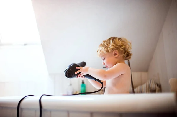 Niño pequeño con secador de pelo en la bañera en el baño . — Foto de Stock