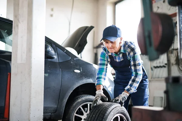 Mecânico feminino sênior reparando um carro em uma garagem . — Fotografia de Stock