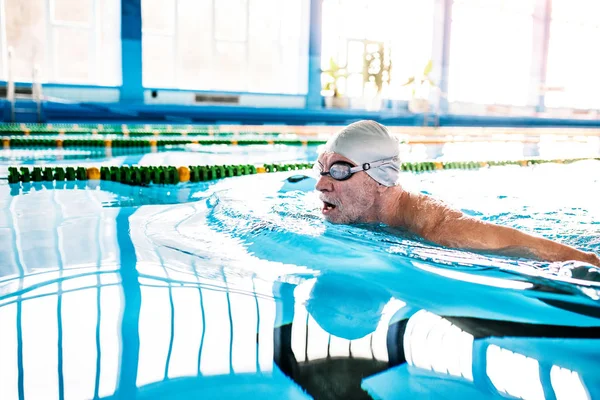 Senior man zwemmen in een overdekt zwembad. — Stockfoto