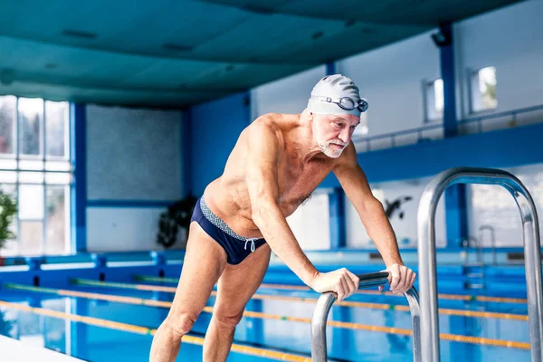 Senior man die zich uitstrekt van het overdekte zwembad. — Stockfoto