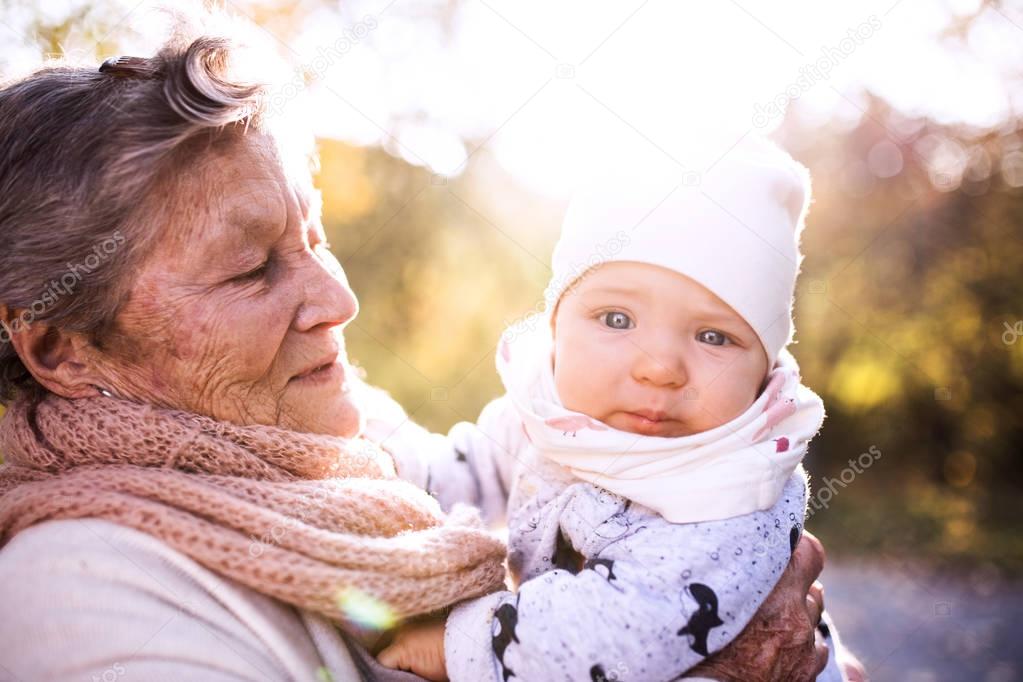 An elderly woman with a baby in autumn nature.