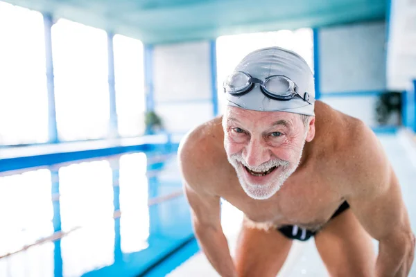 Senior man in een overdekt zwembad. — Stockfoto