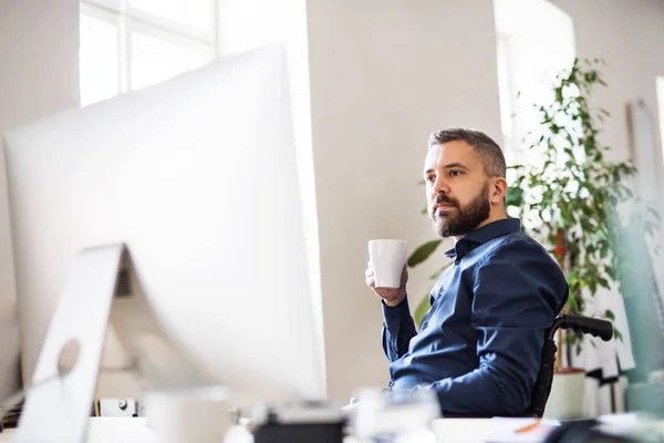 Uomo d'affari in sedia a rotelle alla scrivania nel suo ufficio . — Foto Stock