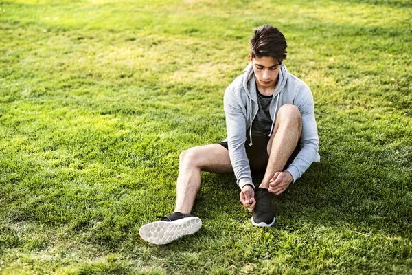 Runner in the city sitting on grass tying shoelaces. — Stock Photo, Image