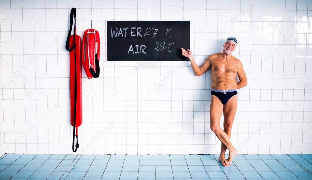 Senior man standing in an indoor swimming pool.