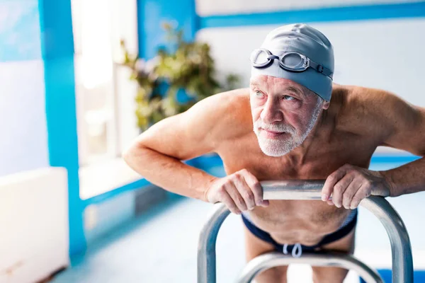 Homem sênior que se estende pela piscina interior . — Fotografia de Stock