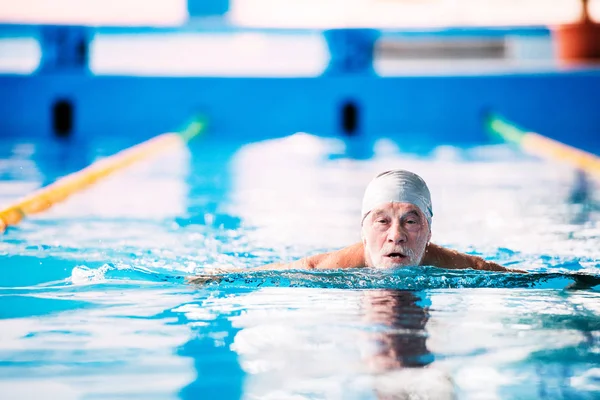 Senior man zwemmen in een overdekt zwembad. — Stockfoto