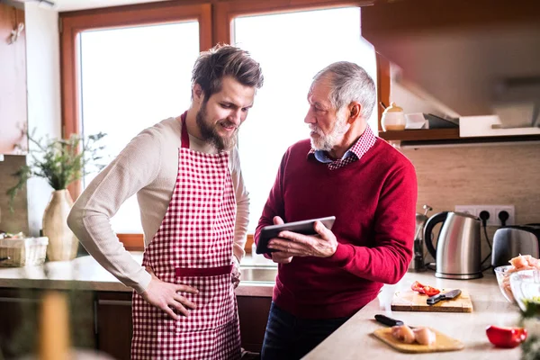 Hipster hijo con su padre mayor con la tableta en la cocina . — Foto de Stock