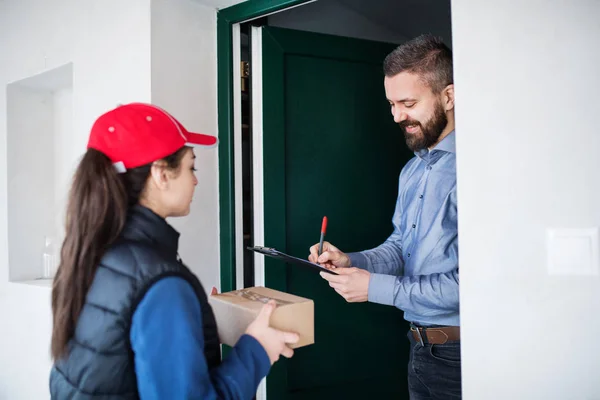 Mann erhält Paket von Zustellerin an der Tür. — Stockfoto