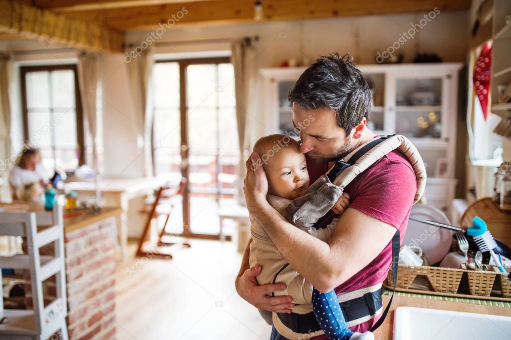 Father with a baby girl in a carrier at home.