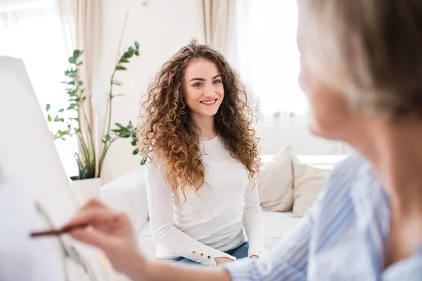 Een senior vrouw schilderij van een tienermeisje thuis. — Stockfoto