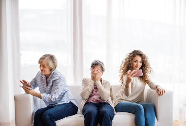 Een tienermeisje, moeder en grootmoeder met smartphone thuis. — Stockfoto