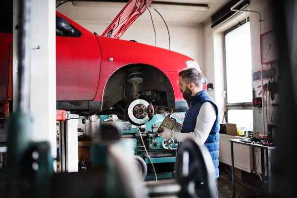 Człowiek mechanik naprawy samochodu w garażu. — Zdjęcie stockowe
