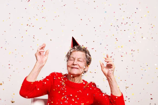 Portrait of a senior woman in studio on a gray background. Party concept. — Stock Photo, Image