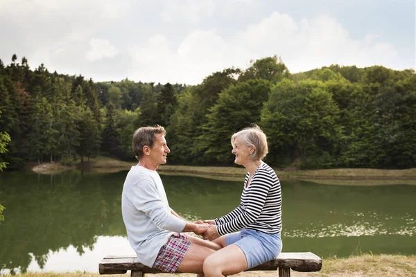 Casal sênior sentado em um banco no lago . — Fotografia de Stock