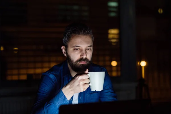 Um homem trabalhando em um laptop em casa à noite . — Fotografia de Stock