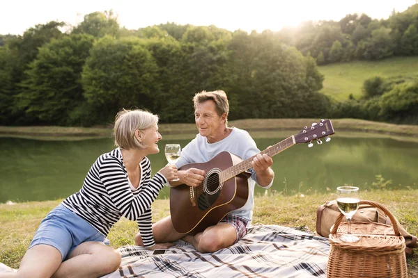 Senior par på søen har en picnic . Royaltyfrie stock-fotos