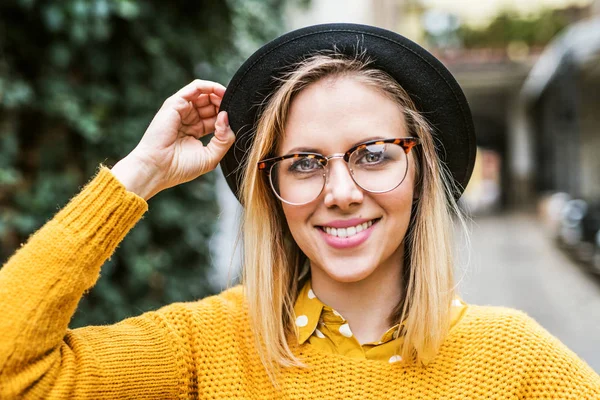 Junge Frau mit schwarzem Hut und Brille in sonniger Frühlingsstadt. — Stockfoto