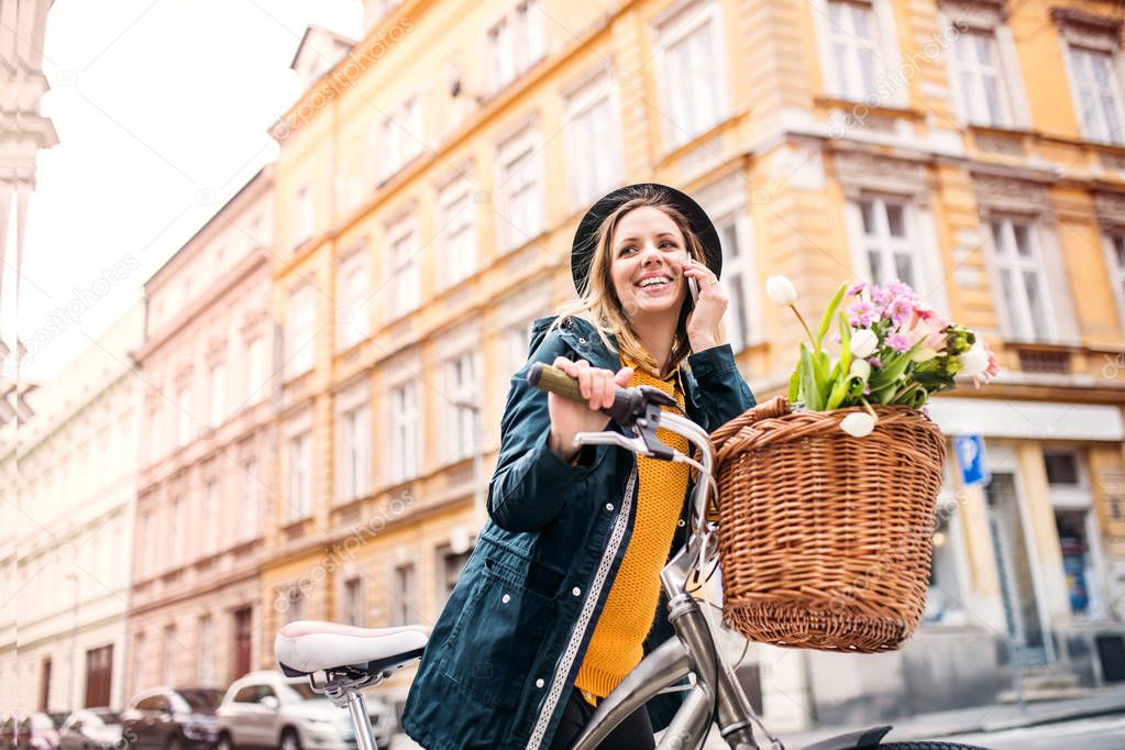 Young woman with bicycle and smartphone in sunny spring town.