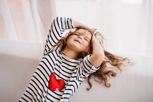 Ein kleines glückliches Mädchen im gestreiften T-Shirt zu Hause, das Spaß hat. — Stockfoto