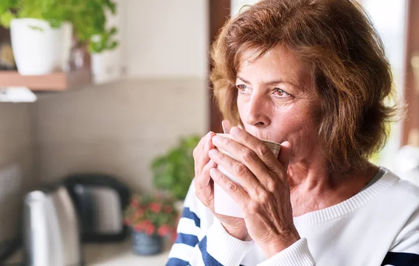 Seniorin hält eine Tasse Kaffee in der Küche. — Stockfoto