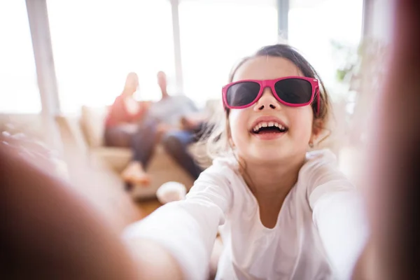 En liten flicka med oigenkännliga föräldrar tar selfie hemma. — Stockfoto