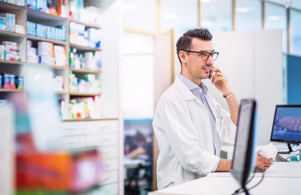 Joven farmacéutico masculino amigable con teléfono inteligente, haciendo una llamada telefónica . —  Fotos de Stock