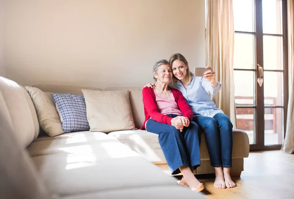 Ältere Großmutter und erwachsene Enkelin mit Smartphone zu Hause. — Stockfoto