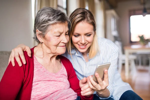 Bejaarde oma en kleindochter van de volwassen met smartphone thuis. — Stockfoto