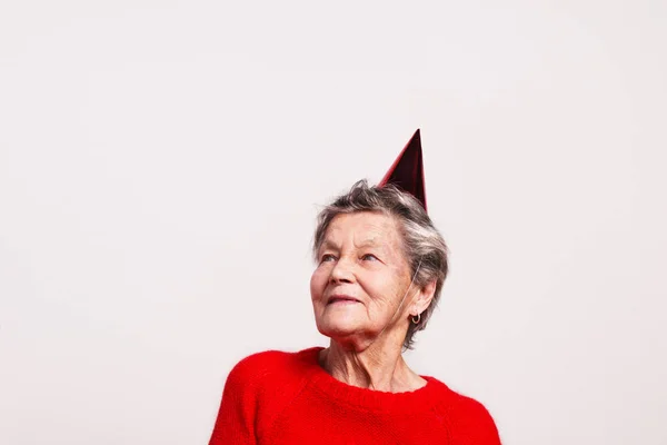 Portrait of a senior woman in studio on a gray background. Party concept. — Stock Photo, Image