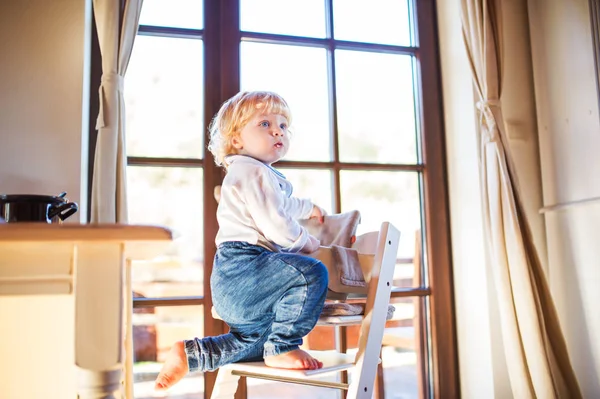 Toddler boy in a dangerous at home, climbing into highchair. — Stock Photo, Image