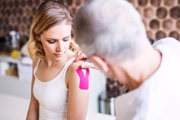 Senior male physiotherapist applying tape on a female patient. — Stock Photo, Image