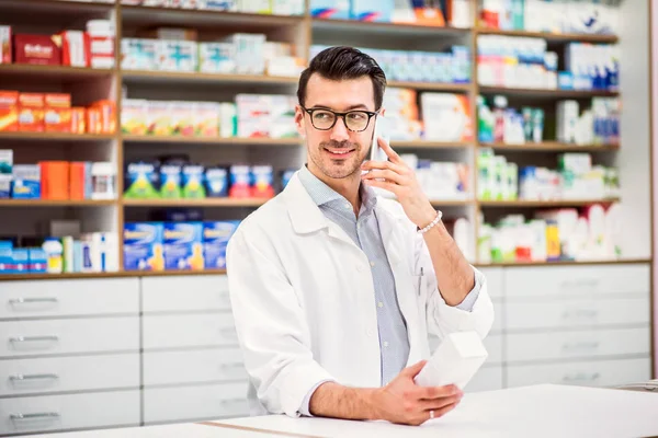 Jovem farmacêutico masculino amigável com smartphone, fazendo um telefonema . — Fotografia de Stock