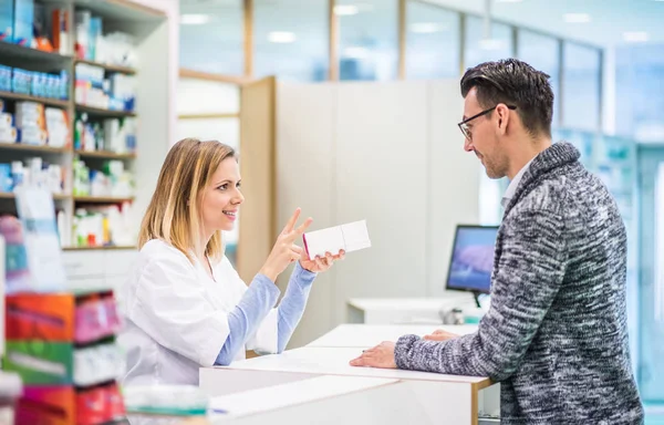 Kvinnliga apotekspersonal som serverar en manlig kund. — Stockfoto