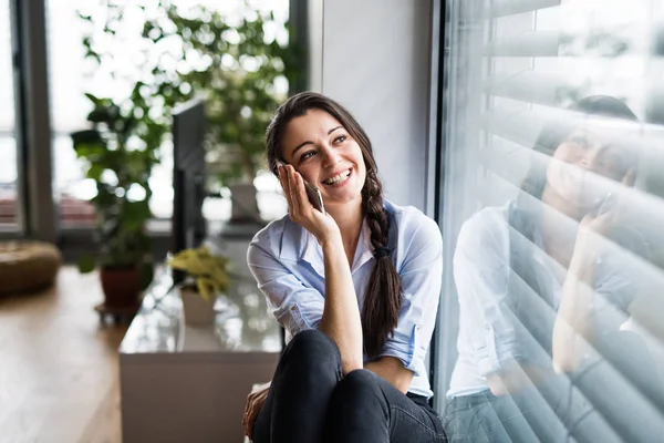 Vrouw met smartphone door het venster thuis, maken een telefoongesprek. — Stockfoto