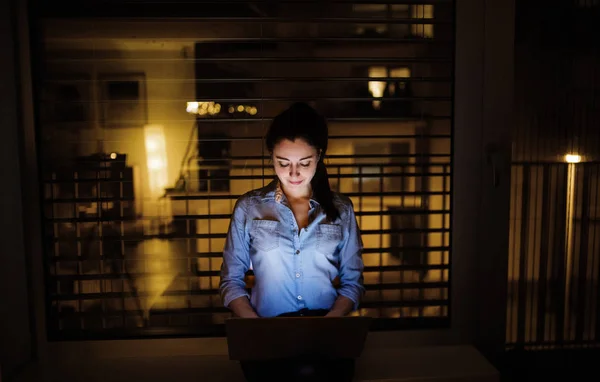 Een vrouw die werken op een laptop thuis of op kantoor bij nacht. — Stockfoto