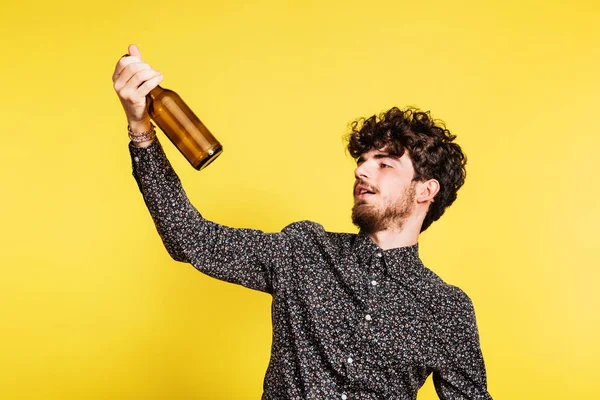 Studio portret van een jonge man met een fles op een gele achtergrond. — Stockfoto