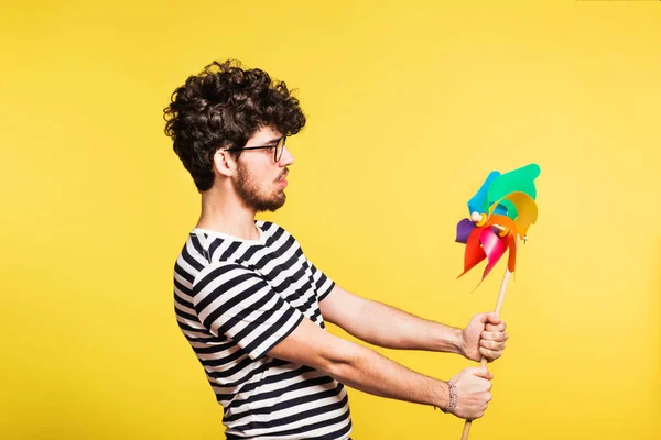 Studio portrait of a young man holding a windmill on a yellow background. — Stock Photo, Image
