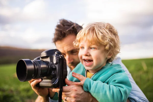 Um pai e seu filho criança com uma câmera fora na natureza primavera . — Fotografia de Stock