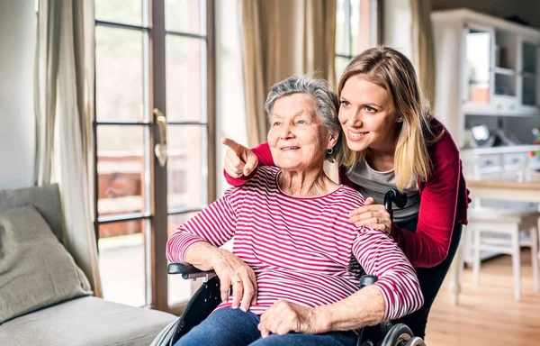 Een bejaarde oma in rolstoel met een volwassen kleindochter thuis. — Stockfoto