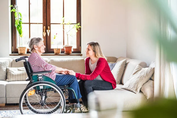 En äldre mormor i rullstol med en vuxen barnbarn hemma. — Stockfoto