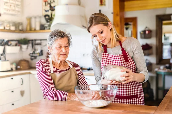 Une grand-mère âgée avec une petite-fille adulte à la maison, cuisiner . — Photo