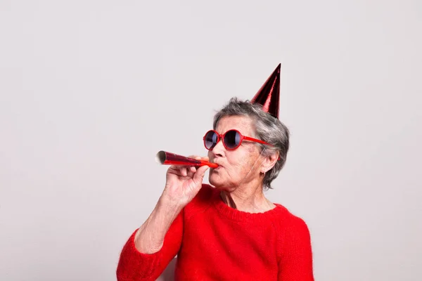 Portrait of a senior woman in studio on a gray background. Party concept. — Stock Photo, Image