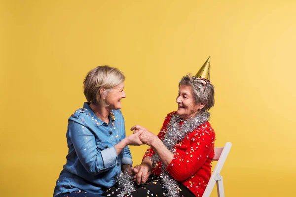 Portrait of a senior women in studio on a yellow background. Party concept. — Stock Photo, Image