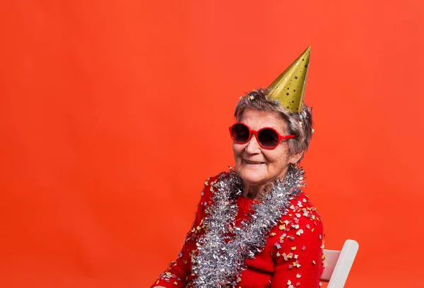 赤い背景のスタジオで年配の女性の肖像画。パーティー コンセプト. — ストック写真