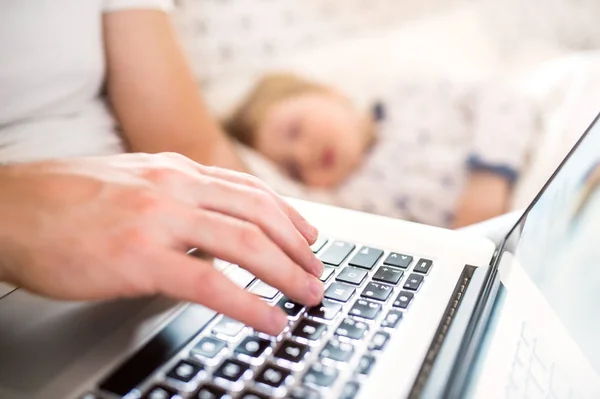 Father with laptop and a sleeping toddler boy in bed at home. — Stock Photo, Image