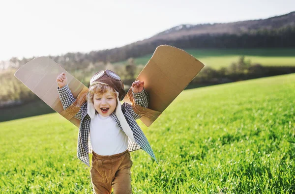 Glada barnet pojke med vingar spelar utanför i vår natur. — Stockfoto