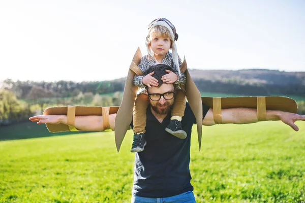 Glada barnet pojke och far spela med vingar utanför i vår natur. — Stockfoto