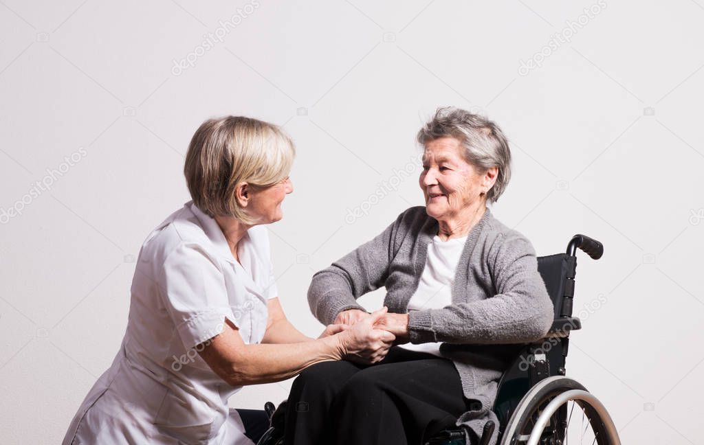 Studio portrait of a senior nurse and an elderly woman in wheelchair.