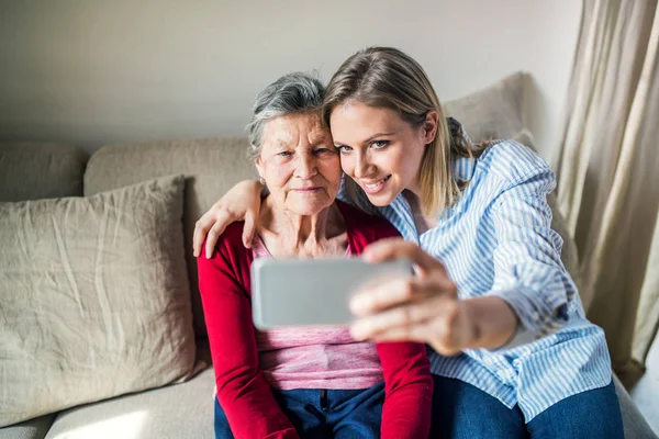 Bejaarde oma en kleindochter van de volwassen met smartphone thuis. — Stockfoto